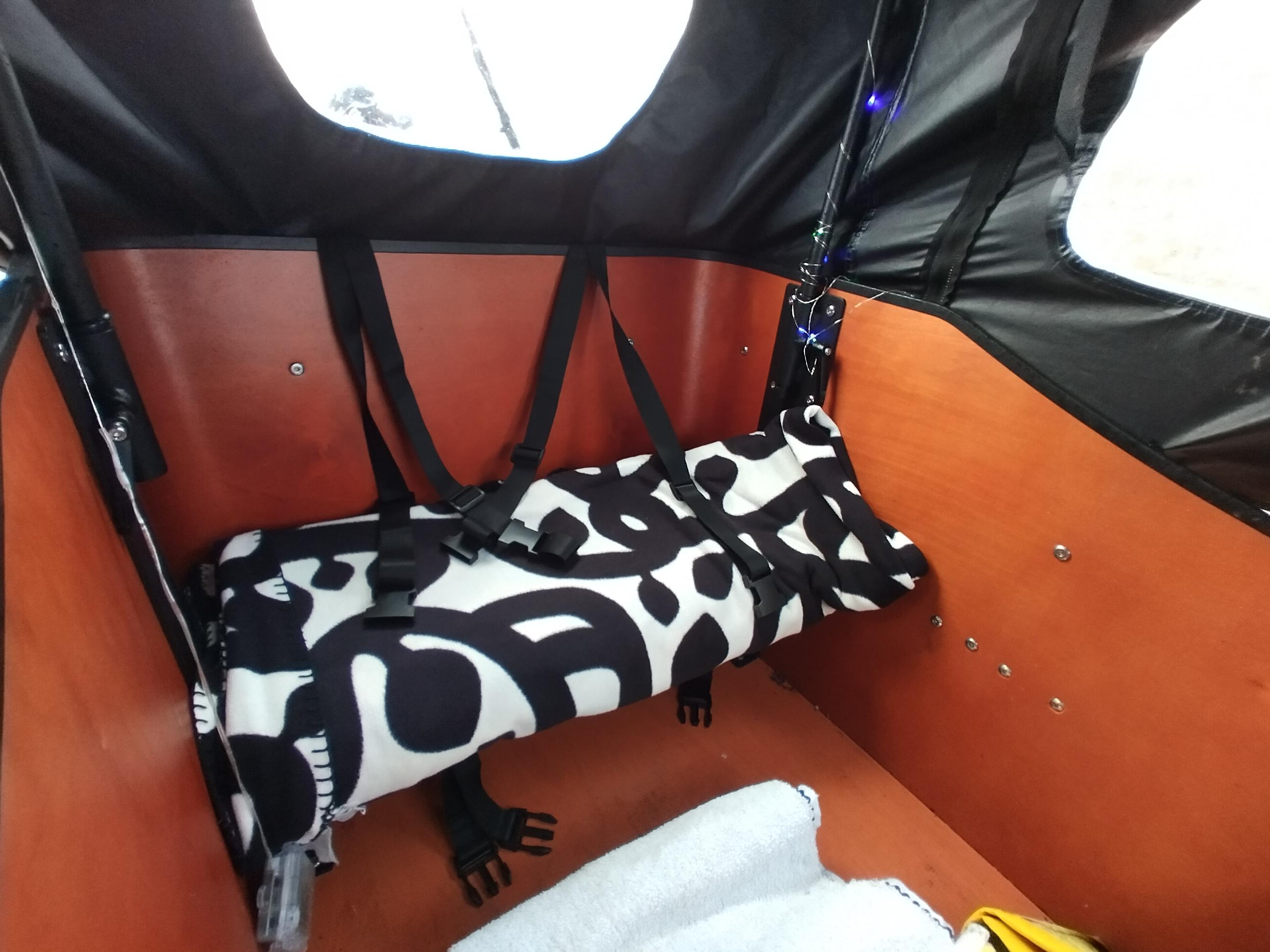 Inside the bucket, with the rain cover on. A fleece blanket lies across the seat.